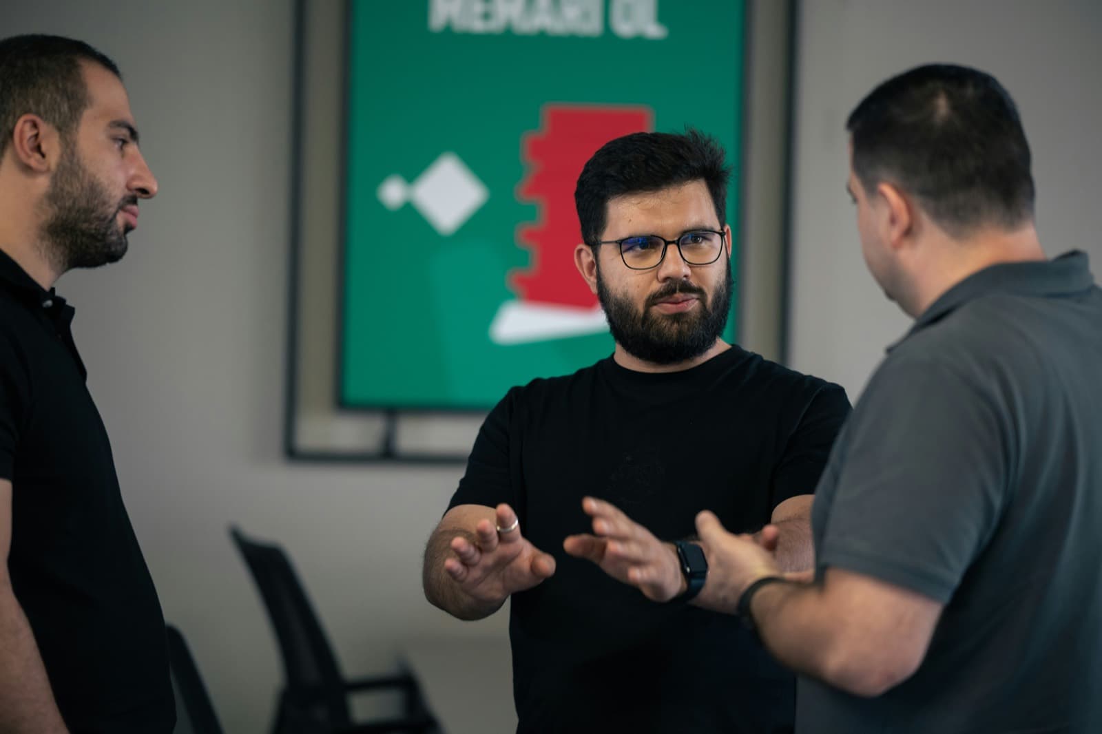 Três profissionais em pé conversando, um deles explicando algo com as mãos